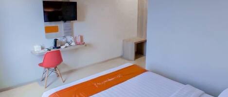 Habitación de hotel con cama, escritorio, silla y televisor montado en la pared.