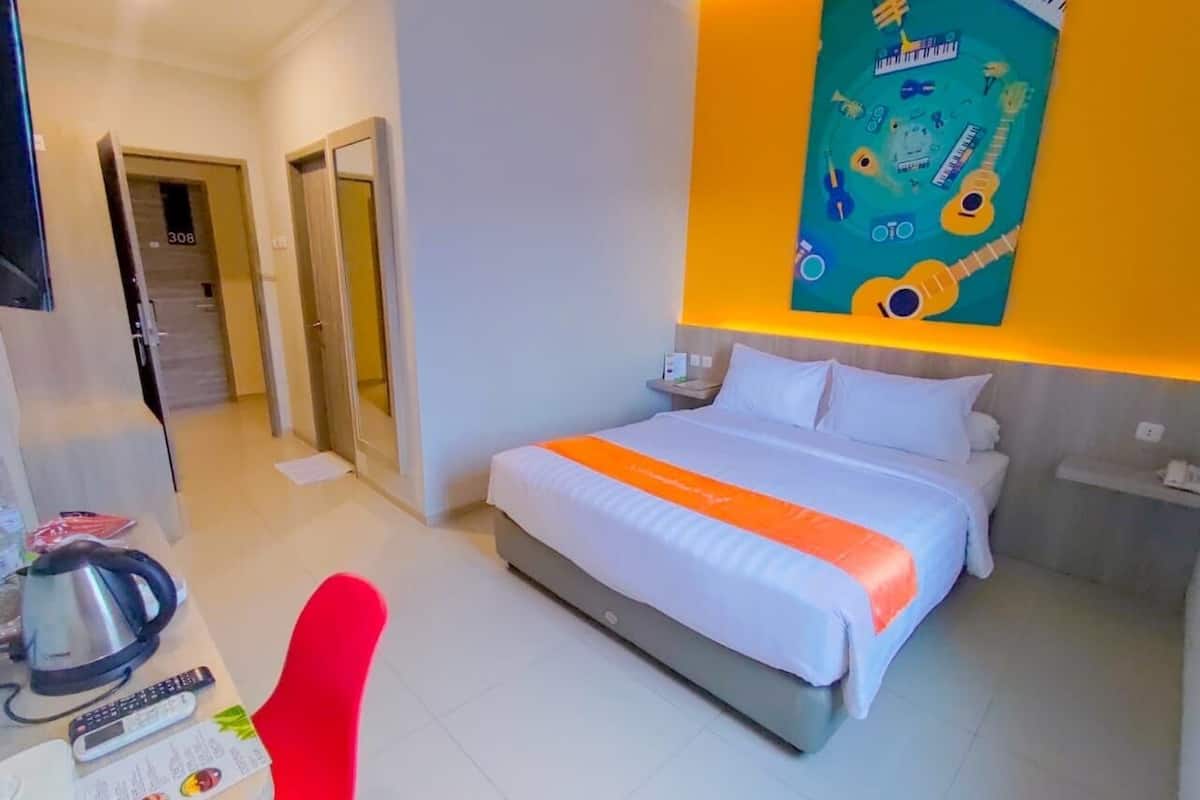 Ein Hotelzimmer mit einem Bett, einem Schreibtisch mit Wasserkocher und einem roten Sessel.