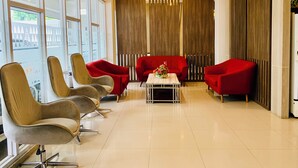 Eine moderne Lobby mit einer Sitzecke, ausgestattet mit roten und beigen Sesseln, einem zentralen Tisch mit einer Vase und einer Holzwand mit vertikalen Lamellen.