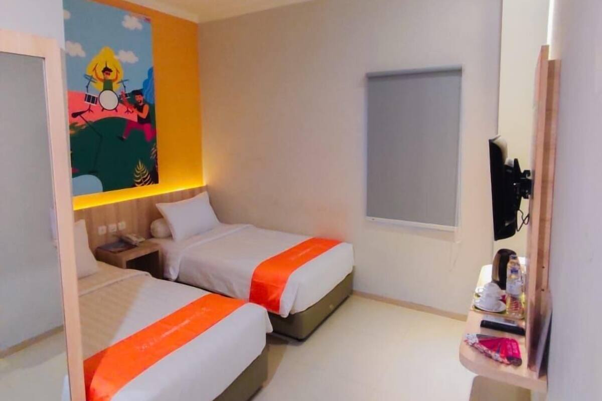 Ein Hotelzimmer mit zwei Betten, einem Bild an der Wand, einem kleinen Fenster und einem Spiegel.