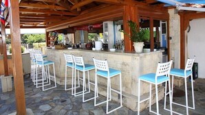 A covered outdoor bar area with stone flooring, white bar stools, and a stone counter. - Mary Anna Villa (Hersonissos)