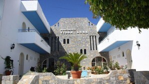 A building with the sign "Apartments Villa Anna" on a stone facade, surrounded by white walls and blue accents, with a palm tree and potted plants in the foreground. - Mary Anna Villa (Hersonissos)