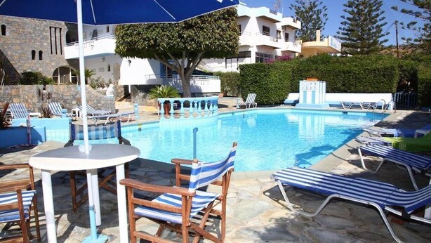 A pool area with lounge chairs and umbrellas, surrounded by stone buildings and greenery. - Mary Anna Villa (Hersonissos)