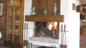 A fireplace with a brick wall and wooden beams, a tiled floor, and a wooden mantelpiece with decorative items. - Razlog Hotel (Razlog)