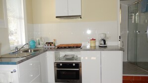 Une cuisine compacte avec des meubles blancs, un four encastré, une machine à café et une porte de douche en verre.