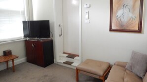 Un salon avec un téléviseur posé sur un meuble, une porte, un tableau accroché au mur et un canapé.