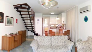 A living room with a sofa, a TV, a wooden cabinet, and a staircase leading to a kitchen area. - Residence Fontana Barone (Cefalù)