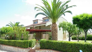 A two-story house with a red roof, surrounded by well-maintained hedges and palm trees. - Residence Fontana Barone (Cefalù)