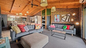 A modern living room with a fireplace, grey sofas, and a herringbone-patterned ottoman. - Black Pearl - Aldinga Beach - C21 SouthCoast Holidays (Aldinga Beach)