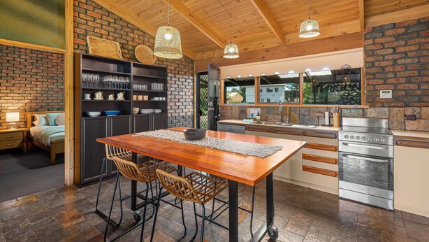 A modern kitchen with a wooden table, bar stools, and a built-in oven. - Black Pearl - Aldinga Beach - C21 SouthCoast Holidays (Aldinga Beach)