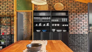 A wooden dining table with a bowl, a black shelf with glassware, and a brick wall. - Black Pearl - Aldinga Beach - C21 SouthCoast Holidays (Aldinga Beach)