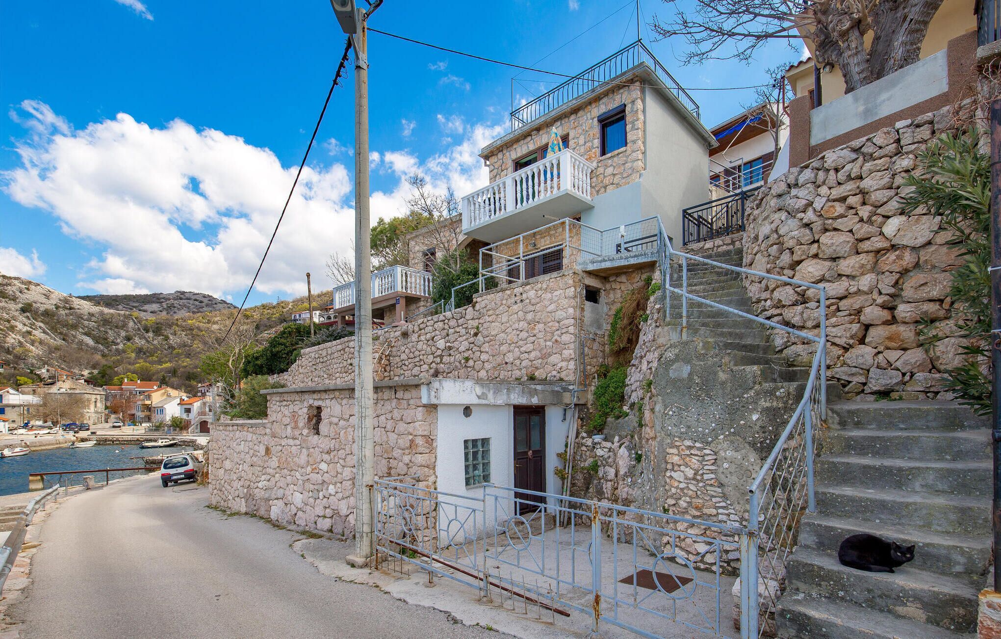 Un edificio costero con muros de piedra, un balcón y una escalera que lleva al piso superior.