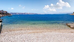 Paesaggio costiero con acqua cristallina, spiaggia di ciottoli e scogliere rocciose.