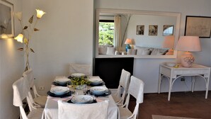 A dining area with a table set for four, white chairs, a vase with flowers, and a mirror above the table reflecting the room. - Sea Front Bonbonnière - Porto Cervo Costa Smeralda (Porto Cervo)