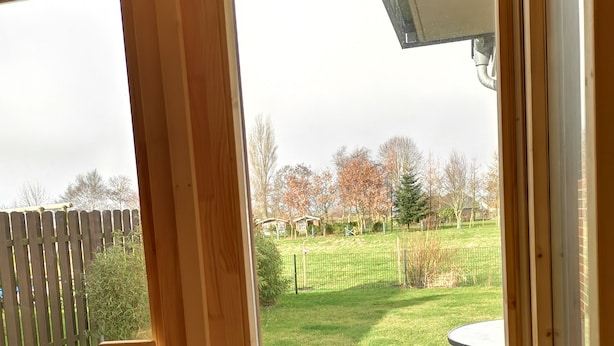 A view through a wooden-framed door to a backyard with a stone wall, a brick patio, and a metal table.