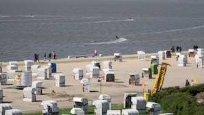 A beach with numerous portable toilets and a few people walking.