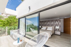 Ein modernes Schlafzimmer mit einem großen Schiebeglasfenster zum Balkon, weißen Korbmöbeln und einer gemusterten Tapete.