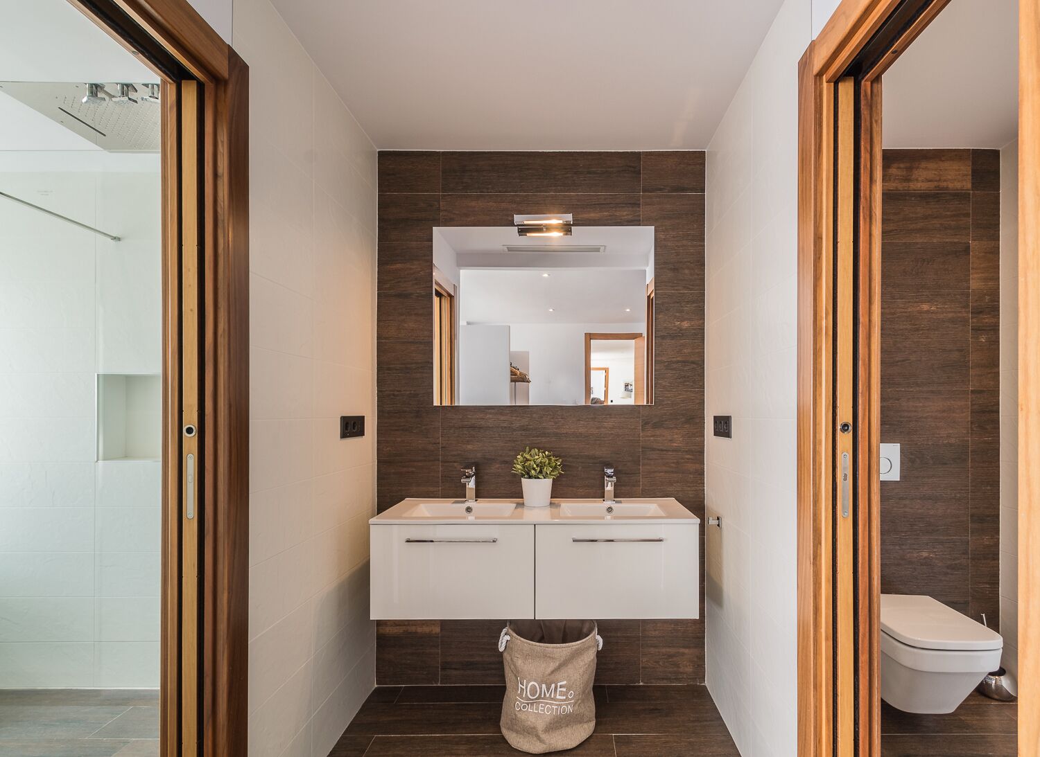 A modern bathroom with a double sink vanity, a large mirror, and a wooden floor.