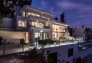 Ein modernes, mehrgeschossiges Haus mit Pool, Sitzgelegenheiten im Freien und einem gut beleuchteten Eingangsbereich.