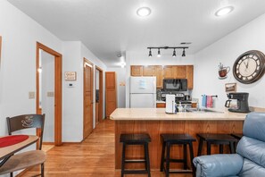Une cuisine moderne avec des meubles en bois, un îlot central, des tabourets de bar et une machine à café.
