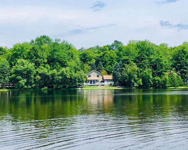 A house by a lake with a dock, surrounded by dense green trees.