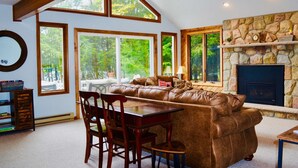 A cozy living room with a stone fireplace, a leather sofa, and a dining area with wooden chairs and a table. - ⛷️⛱️⛰️Family Lake Home❤️3BR★HotTub★Fireplace★Games★Boat/Fish★Dogs+ (Pocono Lake)