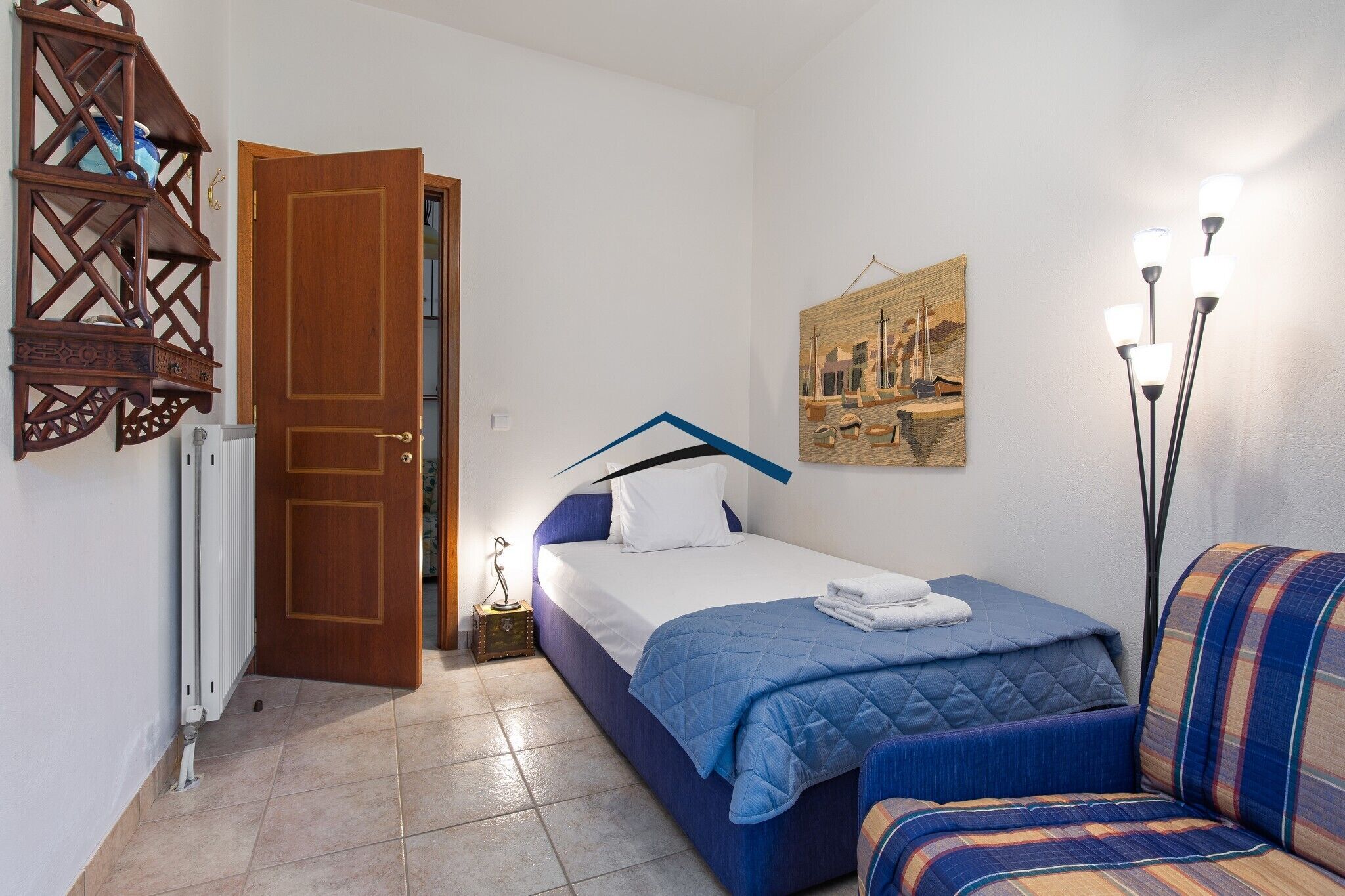 A bedroom with a bed, a chair, a radiator, a door, and a wall-mounted picture.