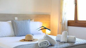 Ein ordentlich bezogenes Bett mit weißen Leinen, einem Strohhut und aufgerollten Handtüchern auf einer gemusterten Tagesdecke.