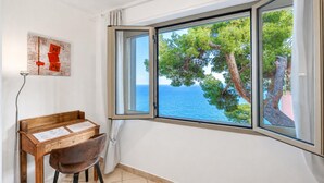A room with a wooden desk, a chair, and a large window with a view of the sea and trees. - Il Suono del Mare - Sea Front (Cervo)