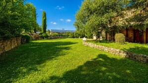 A well-maintained garden with a stone wall, a tall tree, and a building with a red door. - Tenuta Di Litiano Villa With Garden and Pool (Roccastrada)