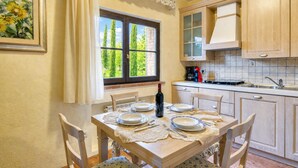 A dining area with a table set for four, a bottle of wine, and a window with a view of trees. - Tenuta Di Litiano Villa With Garden and Pool (Roccastrada)