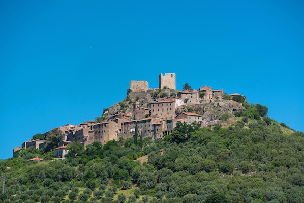 Uma cidade histórica no alto de uma colina, com arquitetura medieval, incluindo uma torre imponente e muralhas fortificadas.