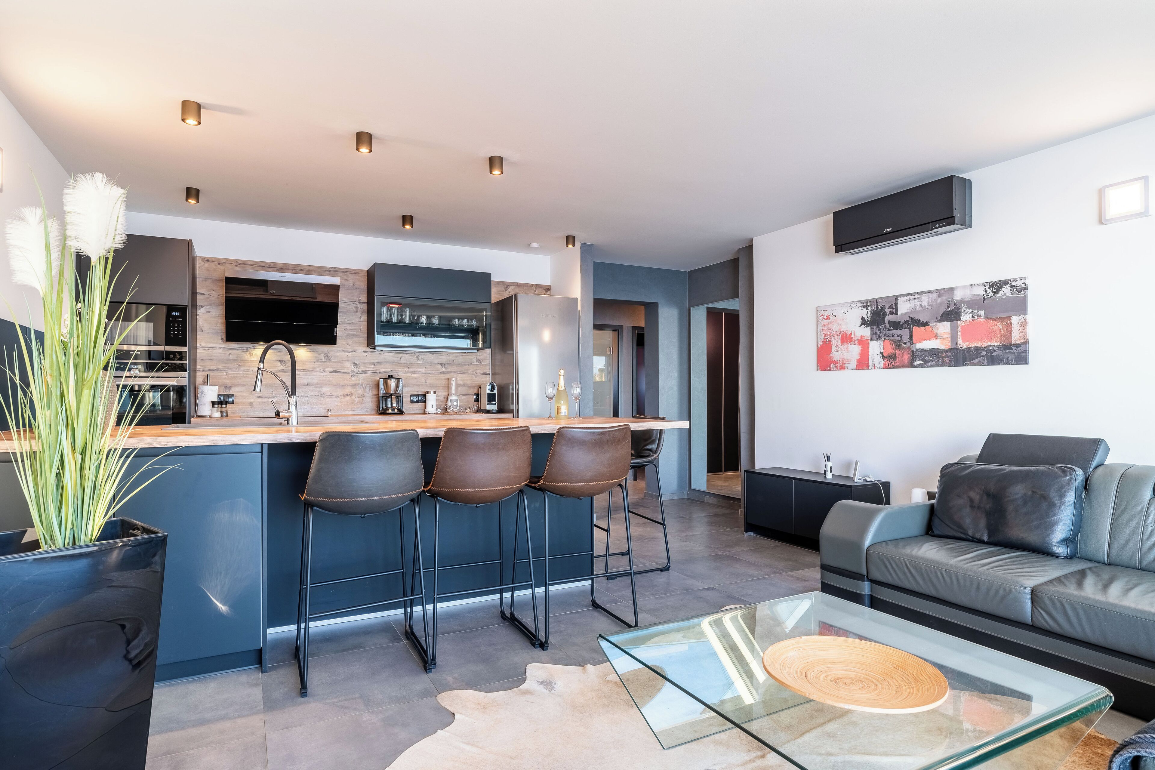 A modern kitchen with a bar area, a dining table, and a leather sofa in a living area.