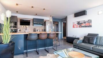 A modern kitchen with a bar area, a dining table, and a leather sofa in a living area.
