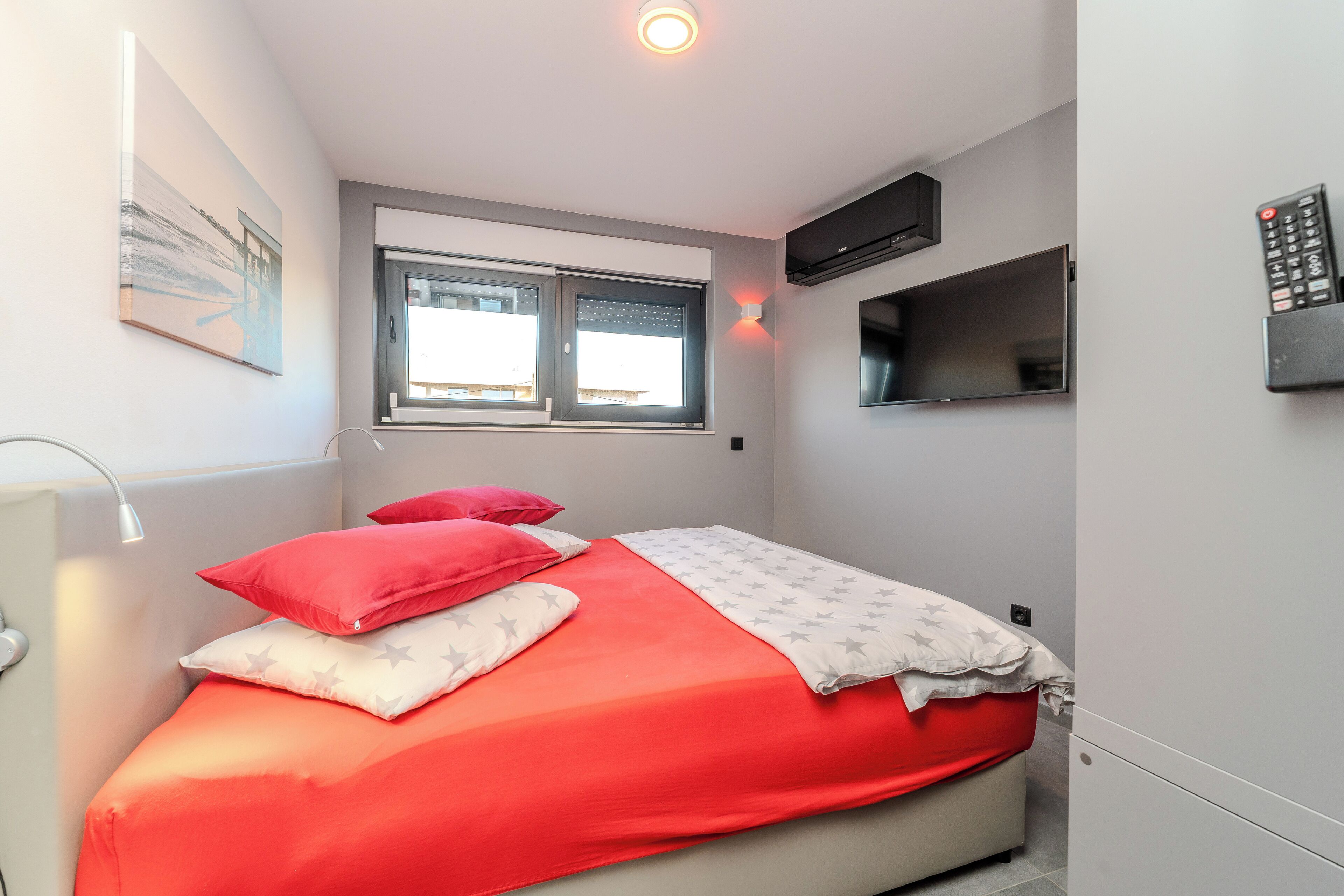 Un dormitorio con cama, ventana, televisor de pared y control remoto.