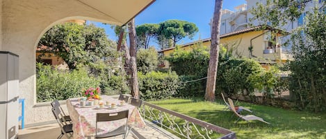 An outdoor patio with a table set for dining, surrounded by a garden and a view of residential buildings.