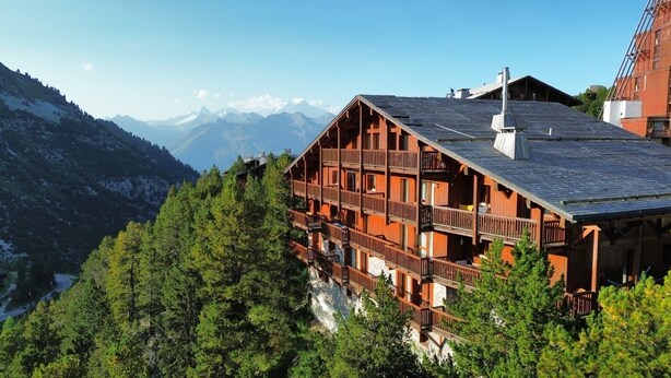 Un chalet en bois doté de plusieurs balcons, situé dans un cadre montagneux.