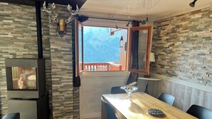 Un salon moderne avec un mur en pierre, une cheminée, un coin repas avec une table et des chaises en bois, et un balcon offrant une vue sur les montagnes.