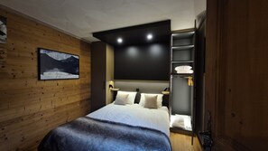 Une chambre moderne avec un mur en bois, un lit recouvert de draps blancs, un tableau accroché au mur et une armoire intégrée dotée d’un miroir.