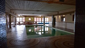 Une piscine dotée d’un sol carrelé, de bancs et offrant une vue sur l’extérieur grâce à de grandes fenêtres.