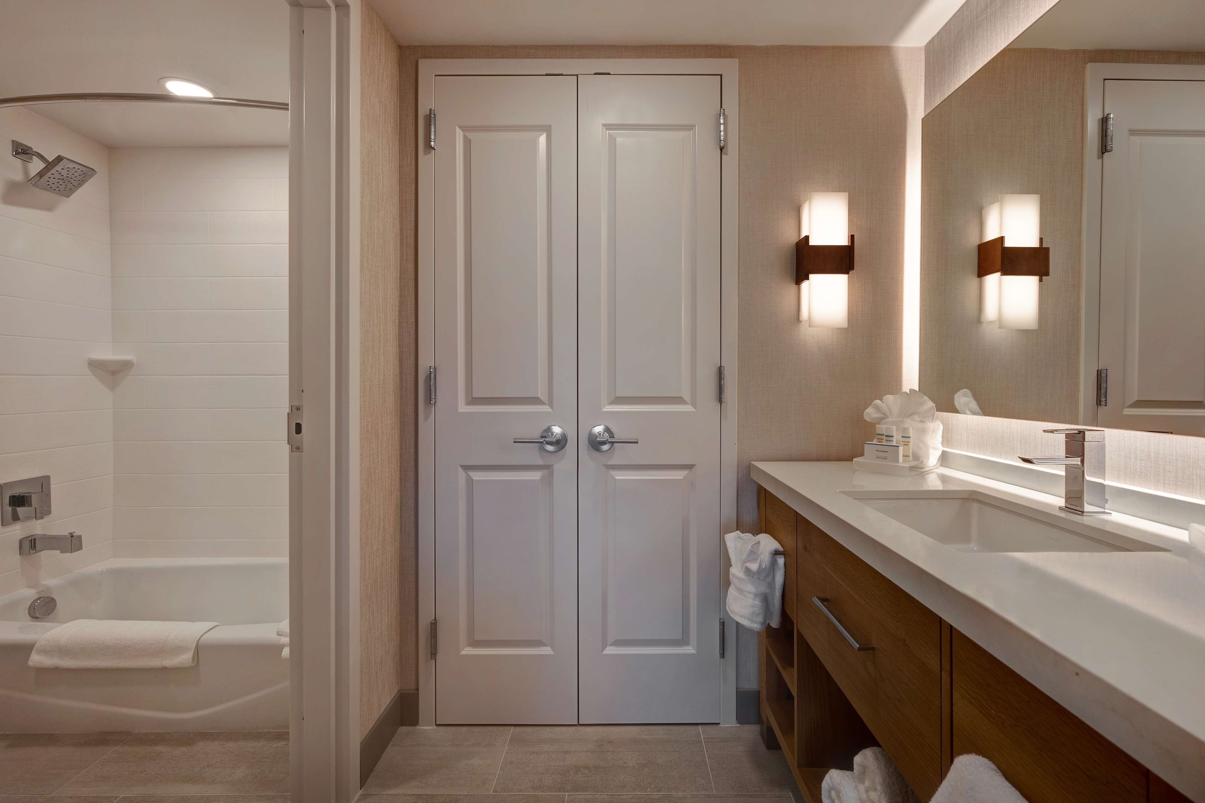 A modern bathroom with a double door, a bathtub, a vanity with a sink, and a mirror.