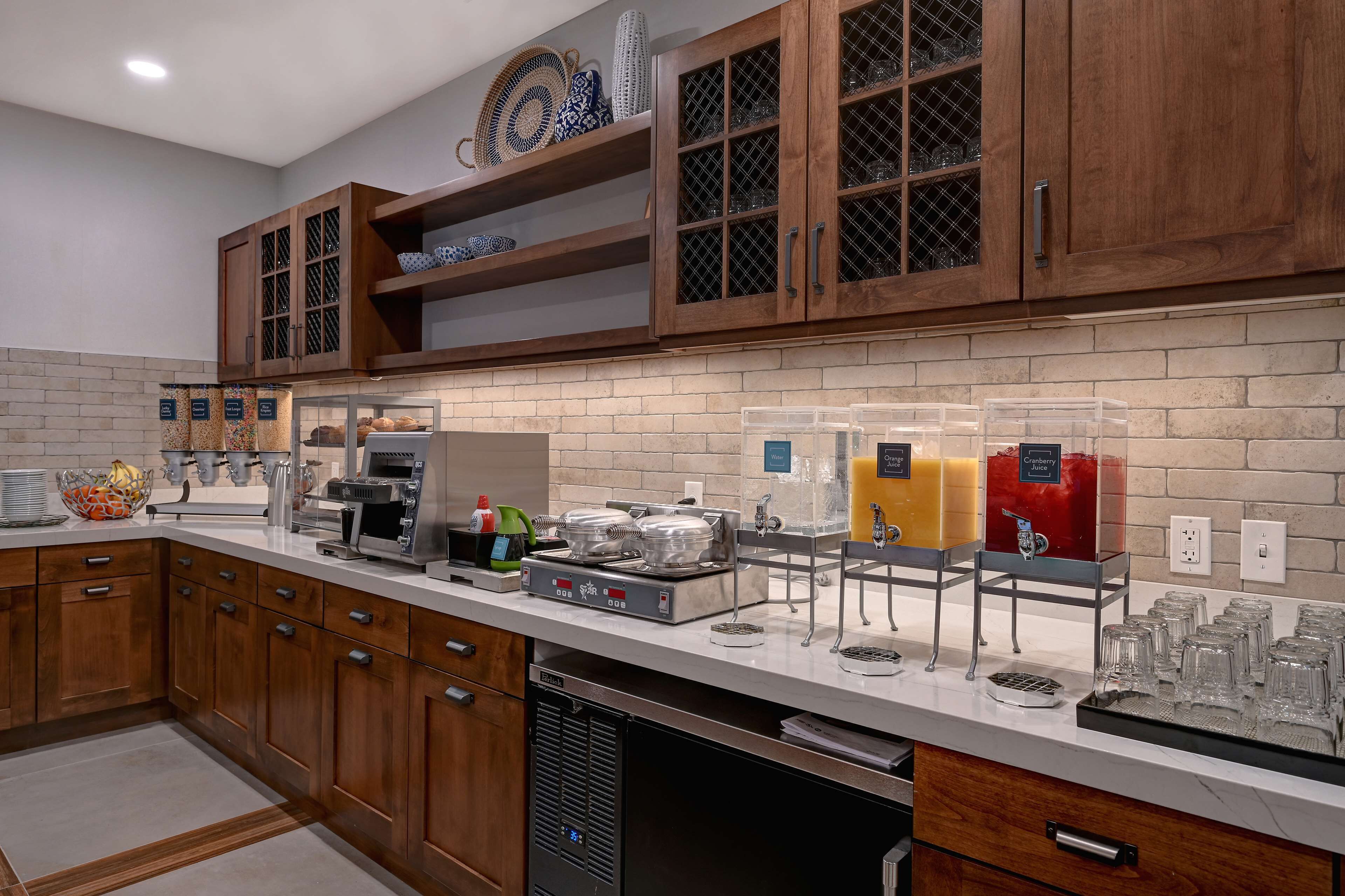 A modern kitchen with wooden cabinets, a brick backsplash, and a coffee station with various beverages.