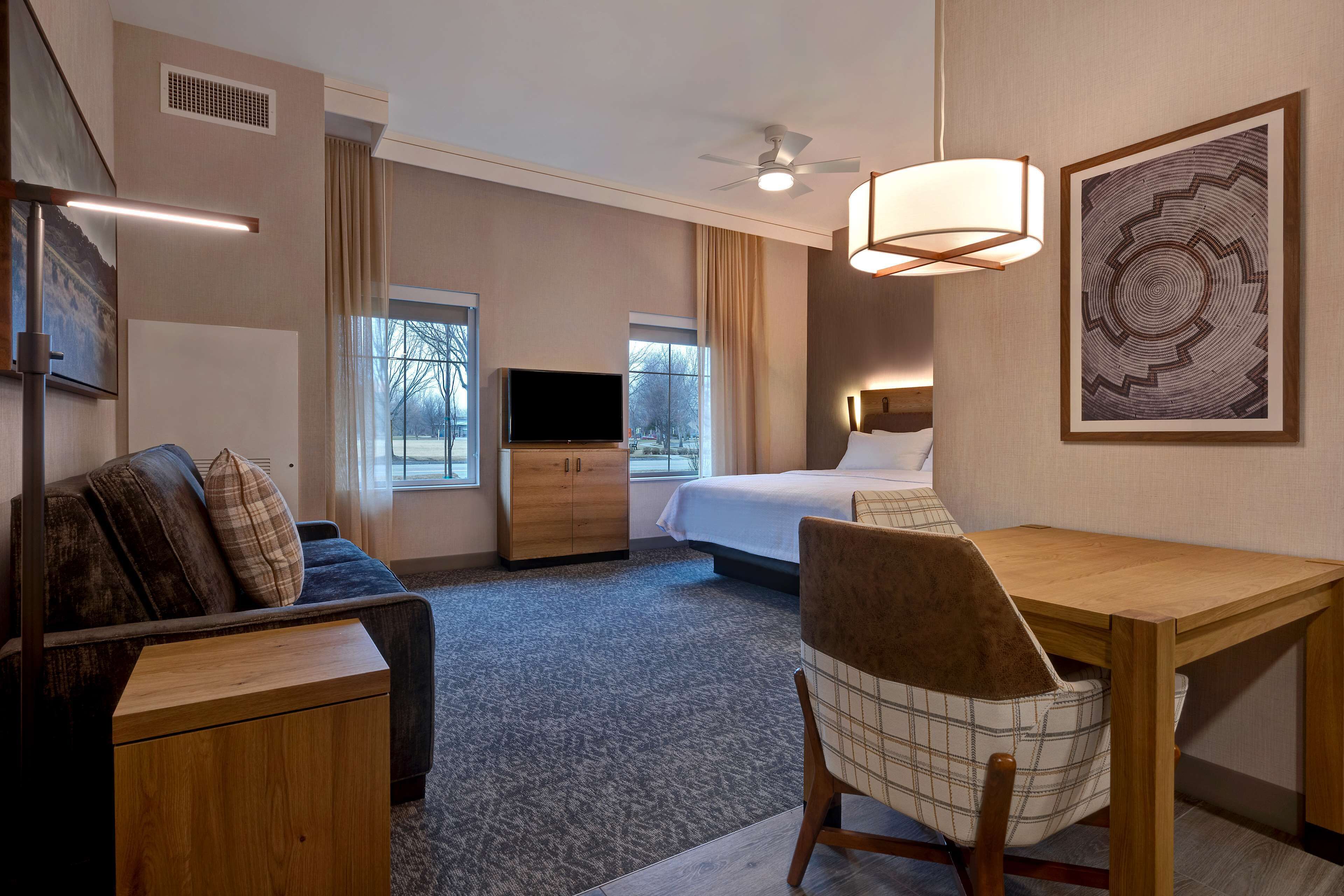 A hotel room with a bed, a desk, a chair, a television, and a ceiling fan.