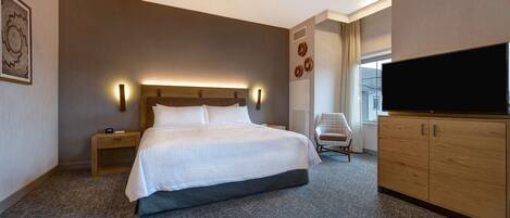 A hotel room with a large bed, a flat-screen TV, a wooden cabinet, a bedside table, and a ceiling fan.