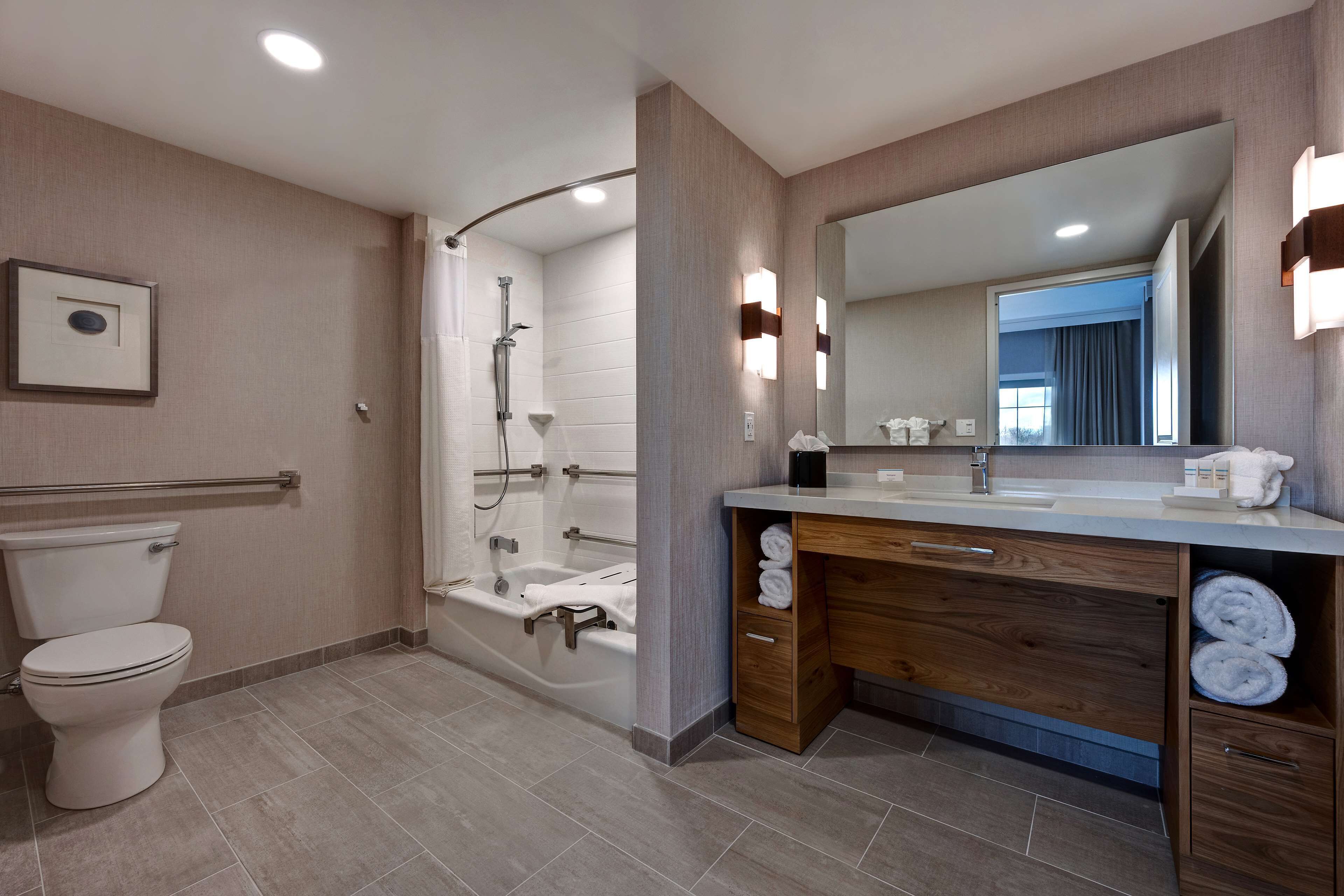 A modern bathroom with a toilet, shower, bathtub, vanity with a mirror, and a towel rack.