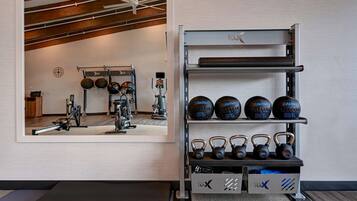 A gym with exercise equipment, a mirrored wall, and a rack with kettlebells and medicine balls.