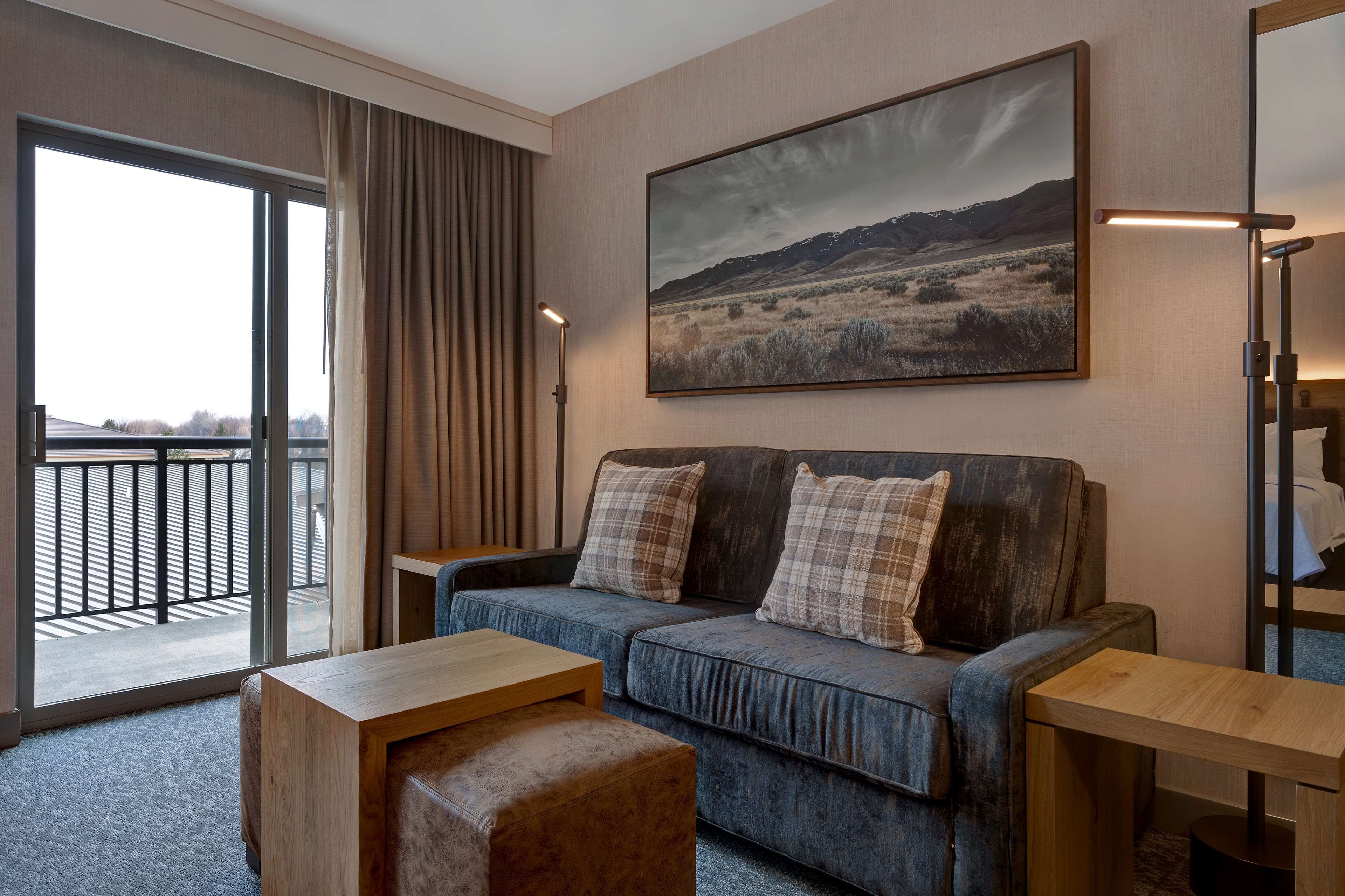 Une chambre d’hôtel avec une grande fenêtre, un canapé, une petite table et un tableau au mur.