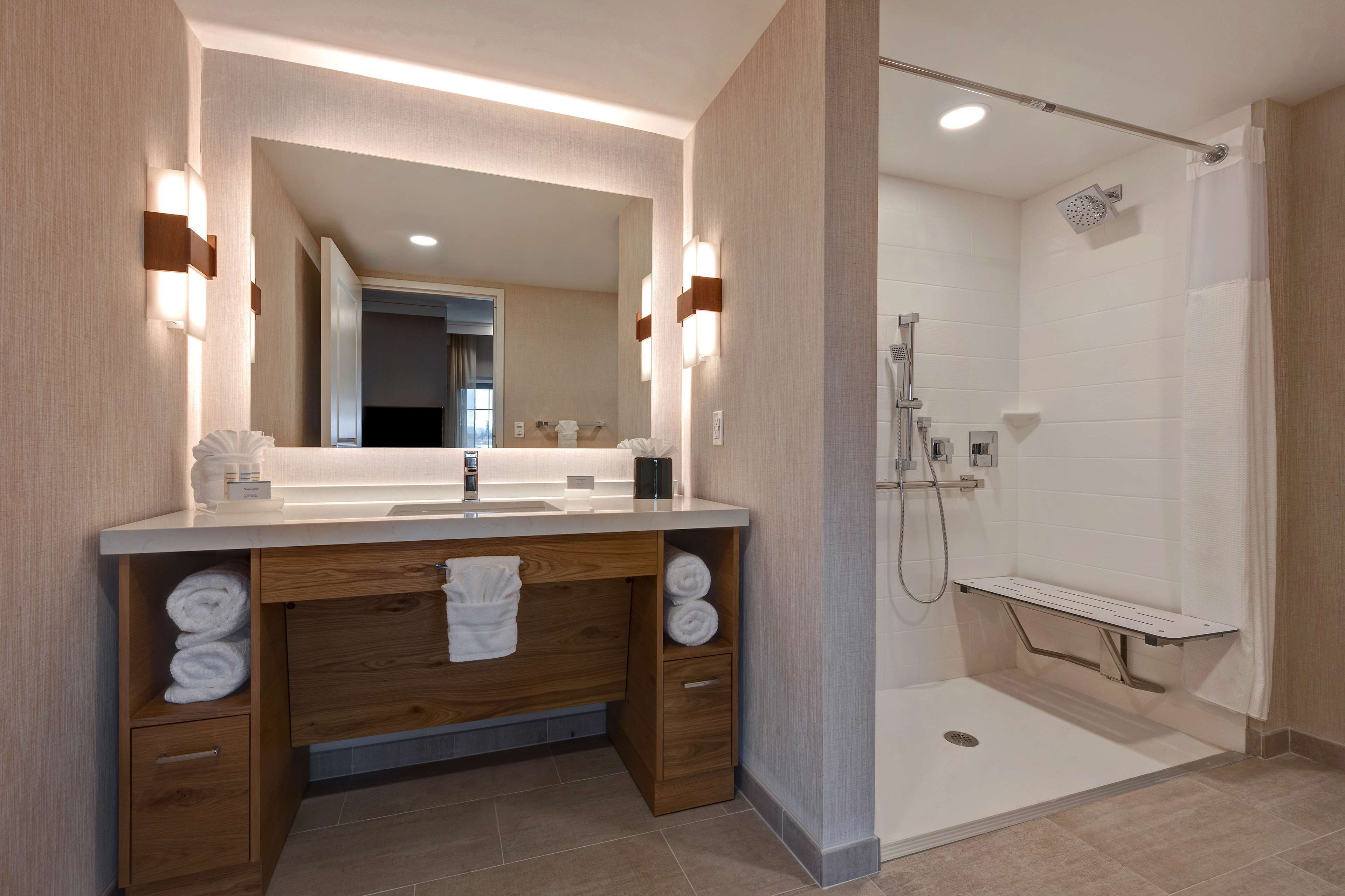 A modern bathroom with a wooden vanity, a large mirror, and a walk-in shower.