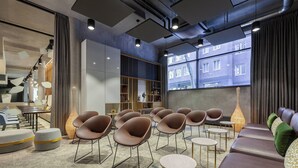Een moderne lounge met zitplaatsen, een boekenkast en een groot raam met uitzicht op gebouwen.