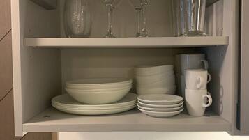Un meuble de cuisine contenant des assiettes blanches, des bols et une pile de tasses blanches.